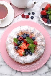 Photo of Tasty Bundt cake with powdered sugar and berries on white marble table, flat lay