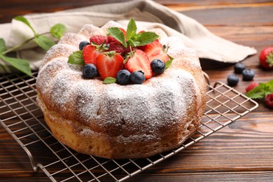 Photo of Tasty Bundt cake with powdered sugar and berries on wooden table, closeup