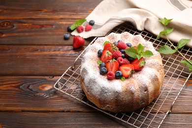 Photo of Tasty Bundt cake with powdered sugar and berries on wooden table, space for text
