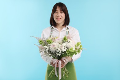 Photo of Florist with beautiful bouquet of flowers on light blue background