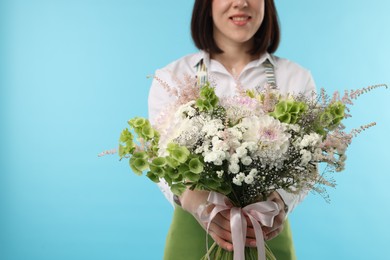 Photo of Florist with beautiful bouquet of flowers on light blue background, closeup. Space for text