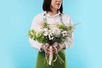 Photo of Florist with beautiful bouquet of flowers on light blue background, closeup