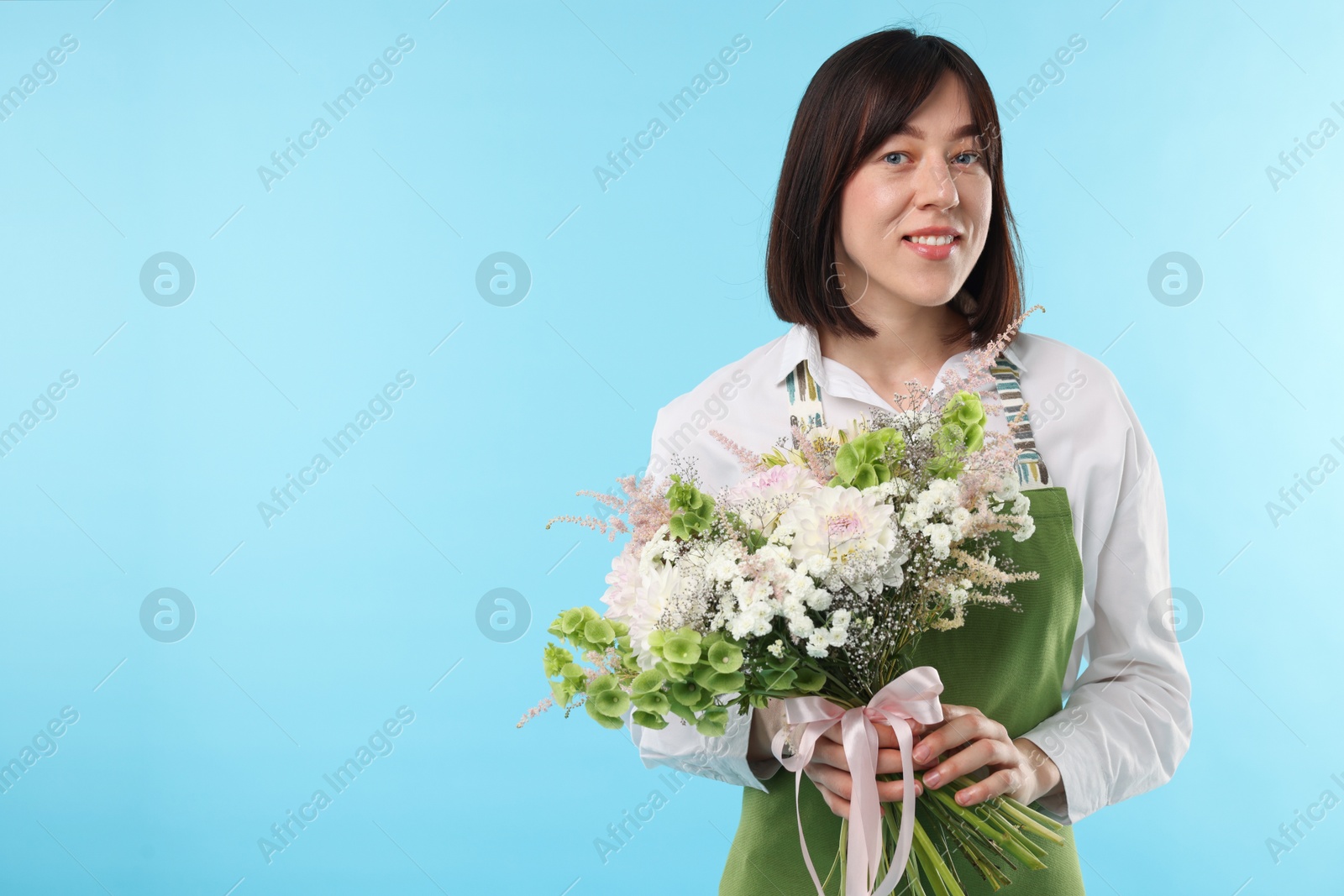 Photo of Florist with beautiful bouquet of flowers on light blue background, space for text