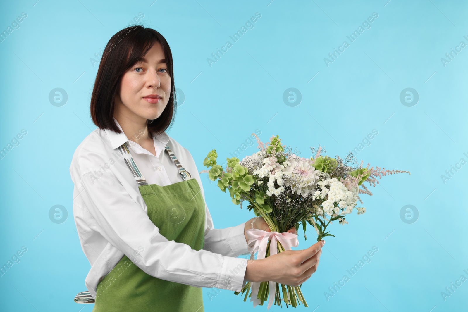Photo of Florist with beautiful bouquet of flowers on light blue background