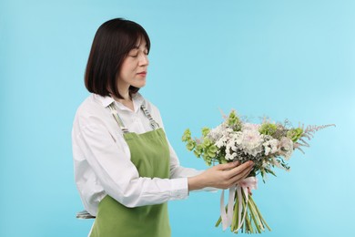 Photo of Florist with beautiful bouquet of flowers on light blue background