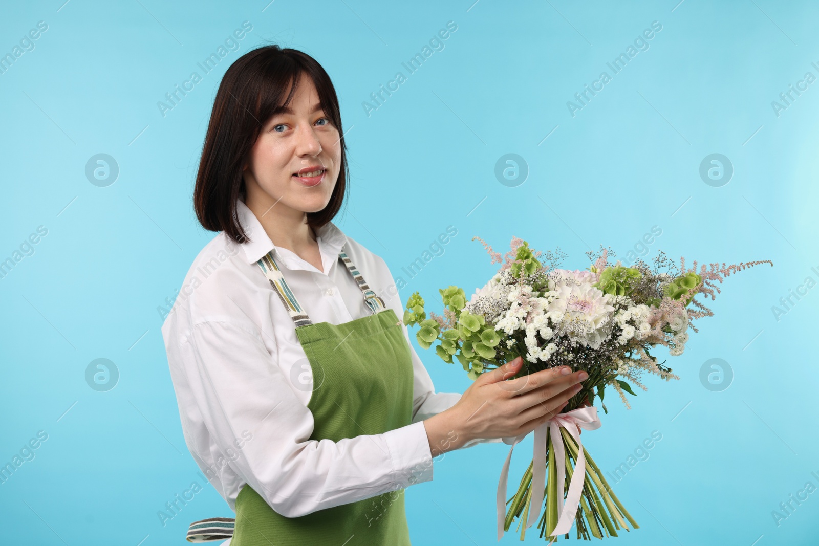 Photo of Florist with beautiful bouquet of flowers on light blue background