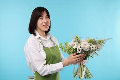 Photo of Florist with beautiful bouquet of flowers on light blue background