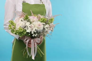Photo of Florist with beautiful bouquet of flowers on light blue background, closeup. Space for text