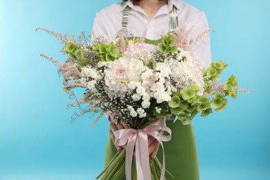 Photo of Florist with beautiful bouquet of flowers on light blue background, closeup