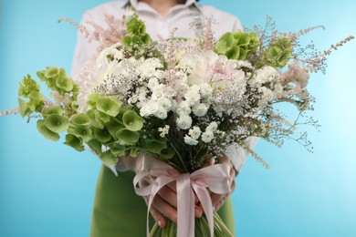 Photo of Florist with beautiful bouquet of flowers on light blue background, closeup