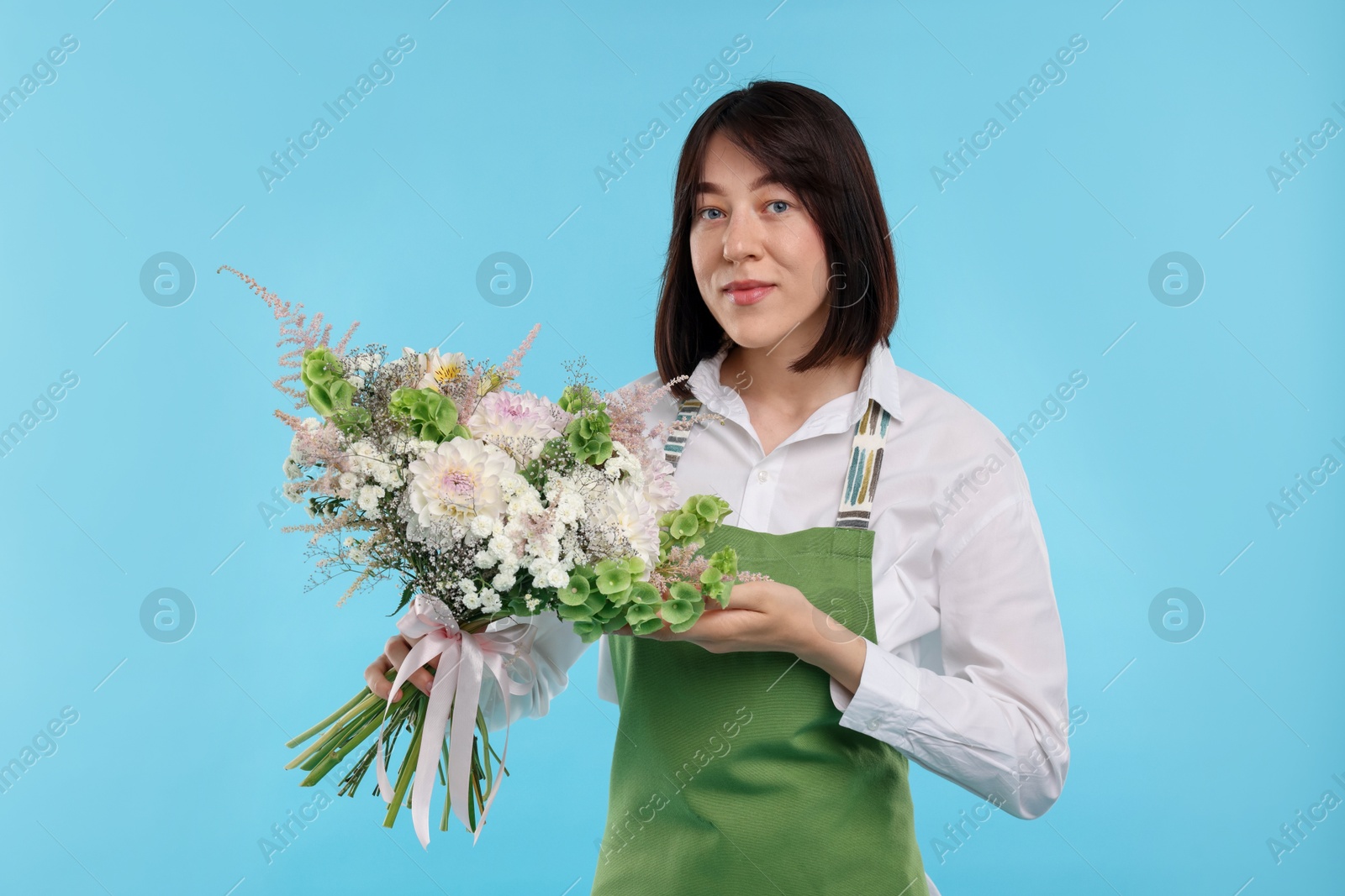 Photo of Florist with beautiful bouquet of flowers on light blue background