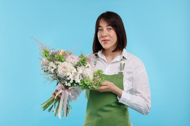 Photo of Florist with beautiful bouquet of flowers on light blue background