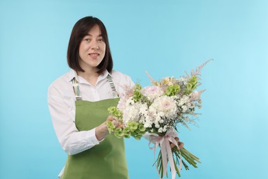 Photo of Florist with beautiful bouquet of flowers on light blue background
