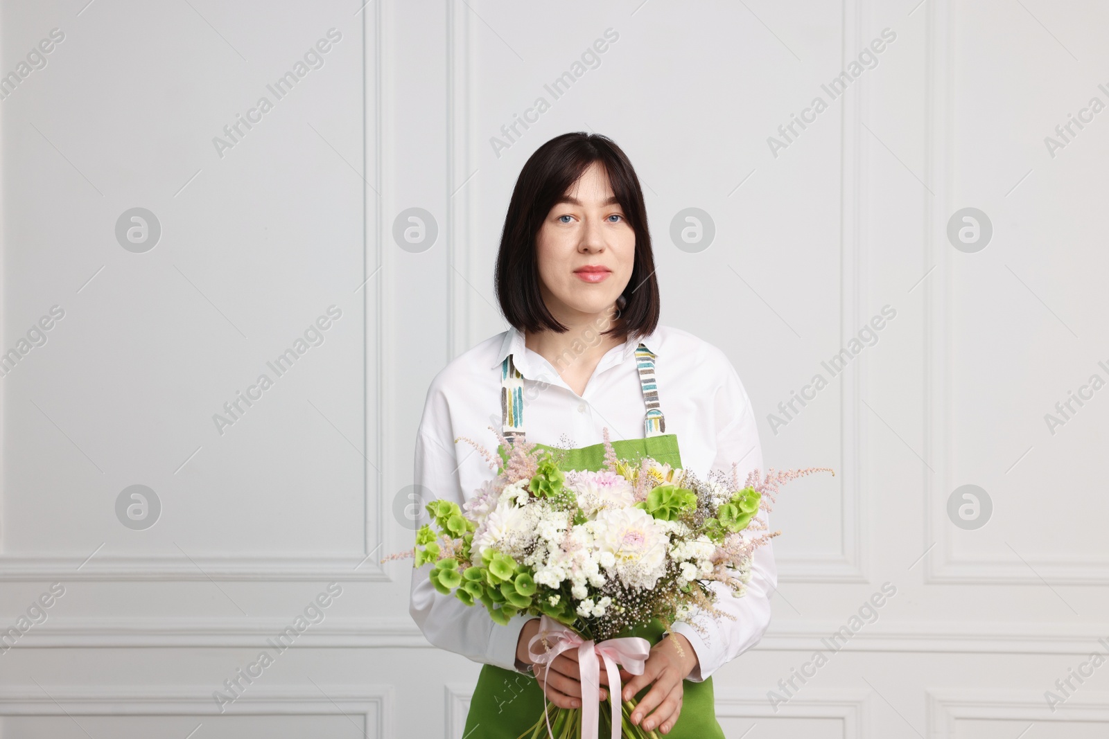 Florist with beautiful bouquet of flowers near white wall indoors Photo of Florist with beautiful bouquet of flowers near white wall indoors