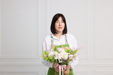 Photo of Florist with beautiful bouquet of flowers near white wall indoors