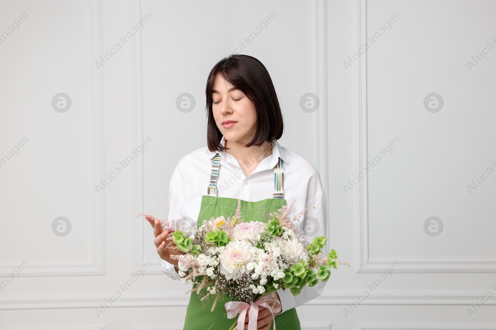 Florist with beautiful bouquet of flowers near white wall indoors Photo of Florist with beautiful bouquet of flowers near white wall indoors