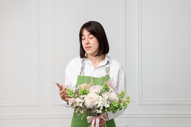 Photo of Florist with beautiful bouquet of flowers near white wall indoors