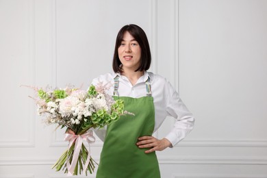Photo of Florist with beautiful bouquet of flowers near white wall indoors