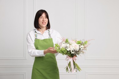 Photo of Florist with beautiful bouquet of flowers near white wall indoors