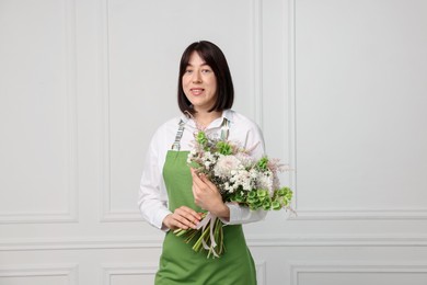 Photo of Florist with beautiful bouquet of flowers near white wall indoors
