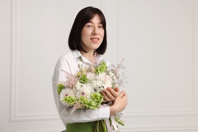 Photo of Florist with beautiful bouquet of flowers near white wall indoors