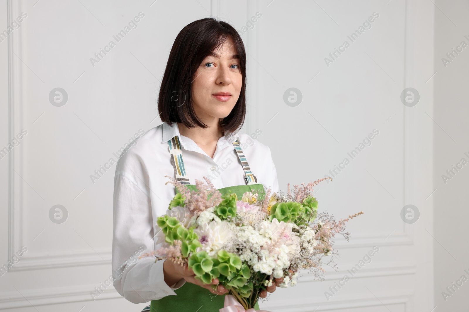 Florist with beautiful bouquet of flowers near white wall indoors Photo of Florist with beautiful bouquet of flowers near white wall indoors