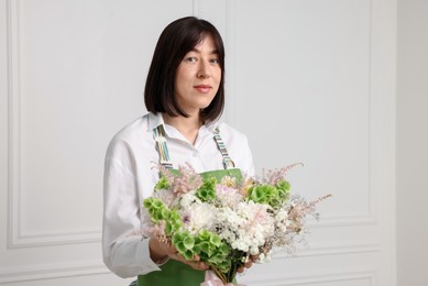 Photo of Florist with beautiful bouquet of flowers near white wall indoors