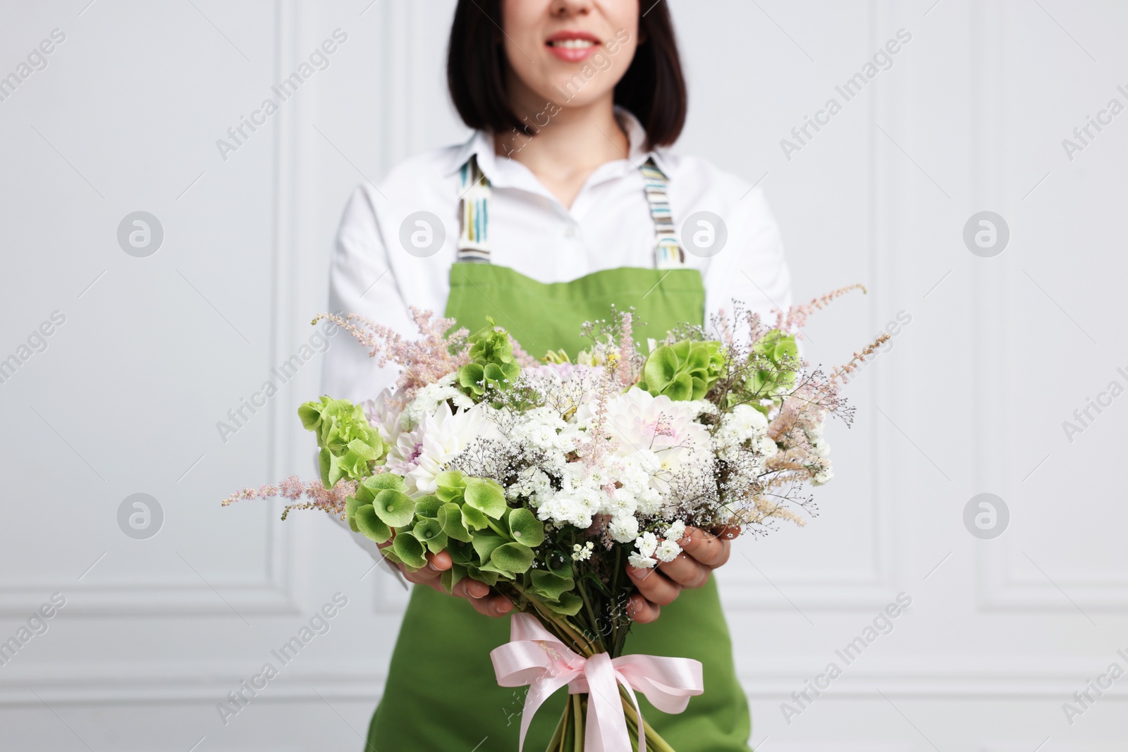 Photo of Florist with beautiful bouquet of flowers near white wall indoors, closeup