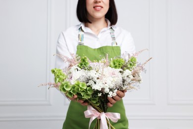 Photo of Florist with beautiful bouquet of flowers near white wall indoors, closeup