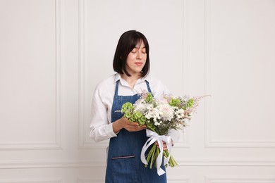 Photo of Florist with beautiful bouquet of flowers near white wall indoors