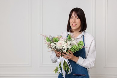 Photo of Florist with beautiful bouquet of flowers near white wall indoors, space for text