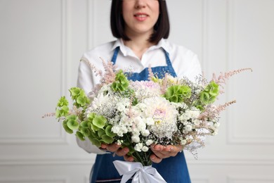 Photo of Florist with beautiful bouquet of flowers near white wall indoors, closeup