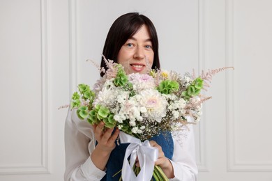 Photo of Florist with beautiful bouquet of flowers near white wall indoors