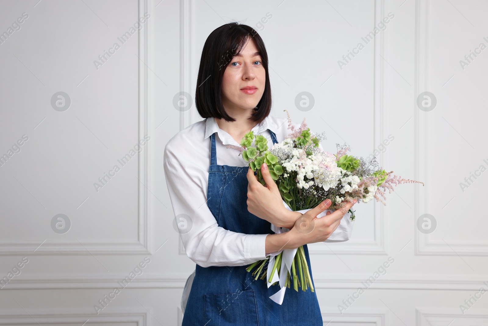 Florist with beautiful bouquet of flowers near white wall indoors Photo of Florist with beautiful bouquet of flowers near white wall indoors