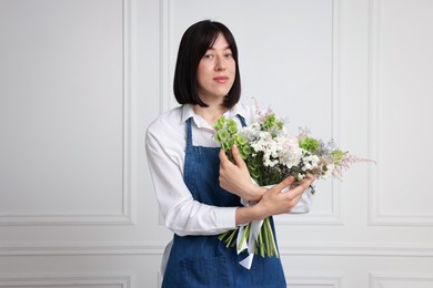 Photo of Florist with beautiful bouquet of flowers near white wall indoors
