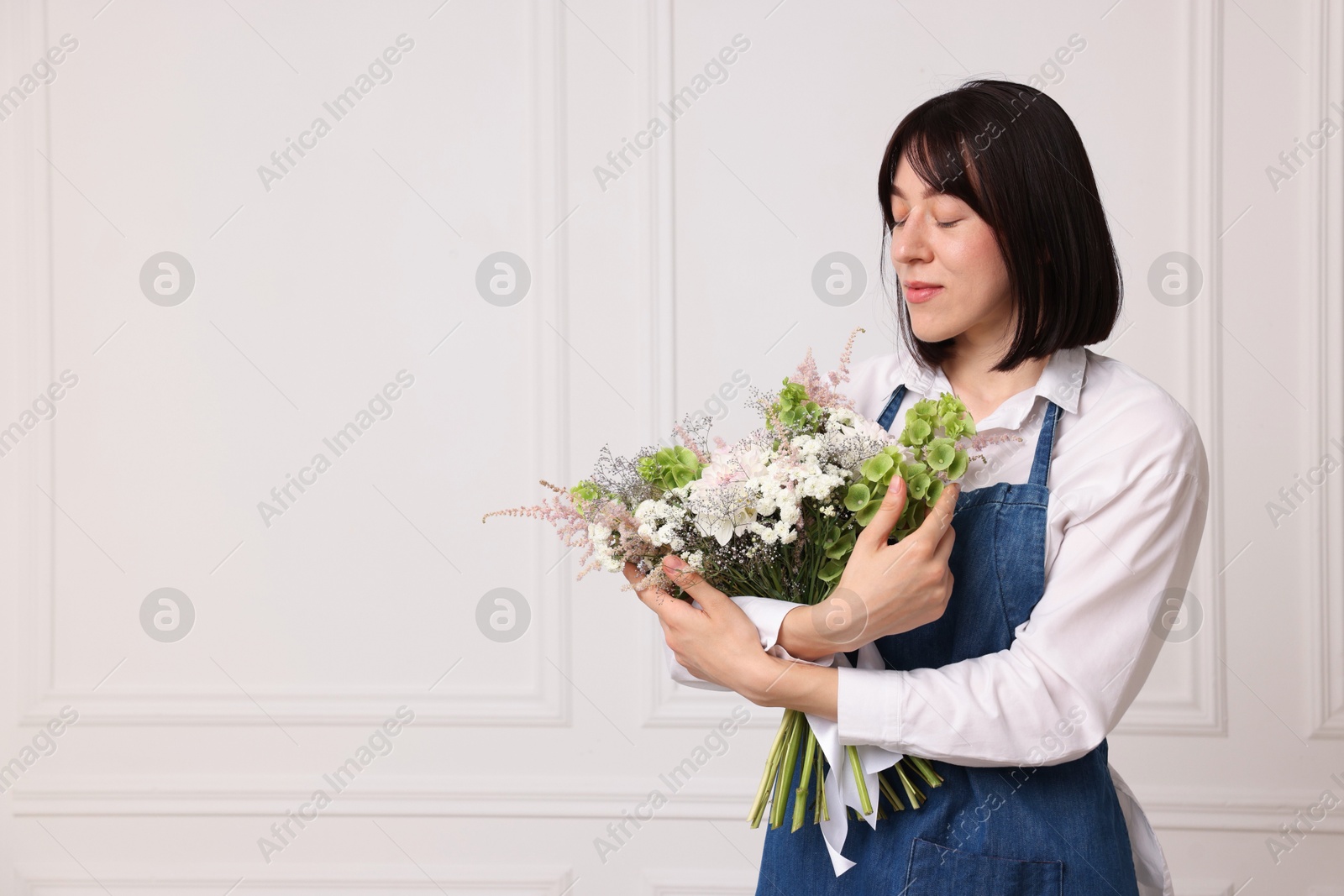 Photo of Florist with beautiful bouquet of flowers near white wall indoors, space for text