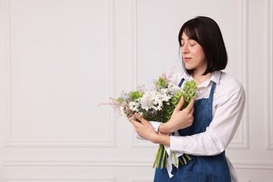 Photo of Florist with beautiful bouquet of flowers near white wall indoors, space for text