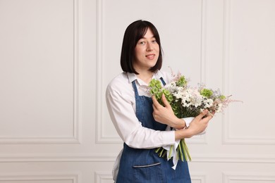 Photo of Florist with beautiful bouquet of flowers near white wall indoors