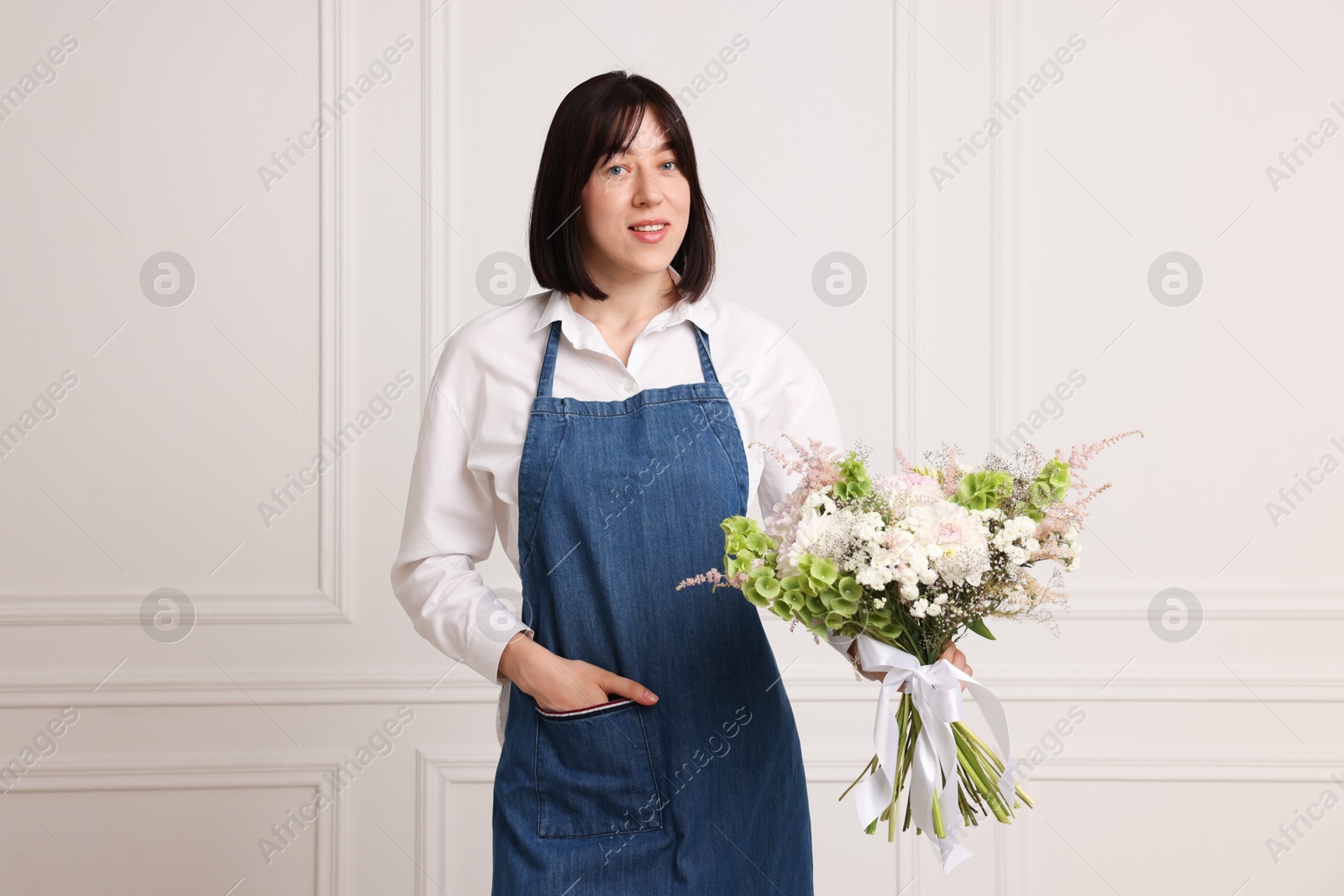 Photo of Florist with beautiful bouquet of flowers near white wall indoors