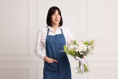 Photo of Florist with beautiful bouquet of flowers near white wall indoors