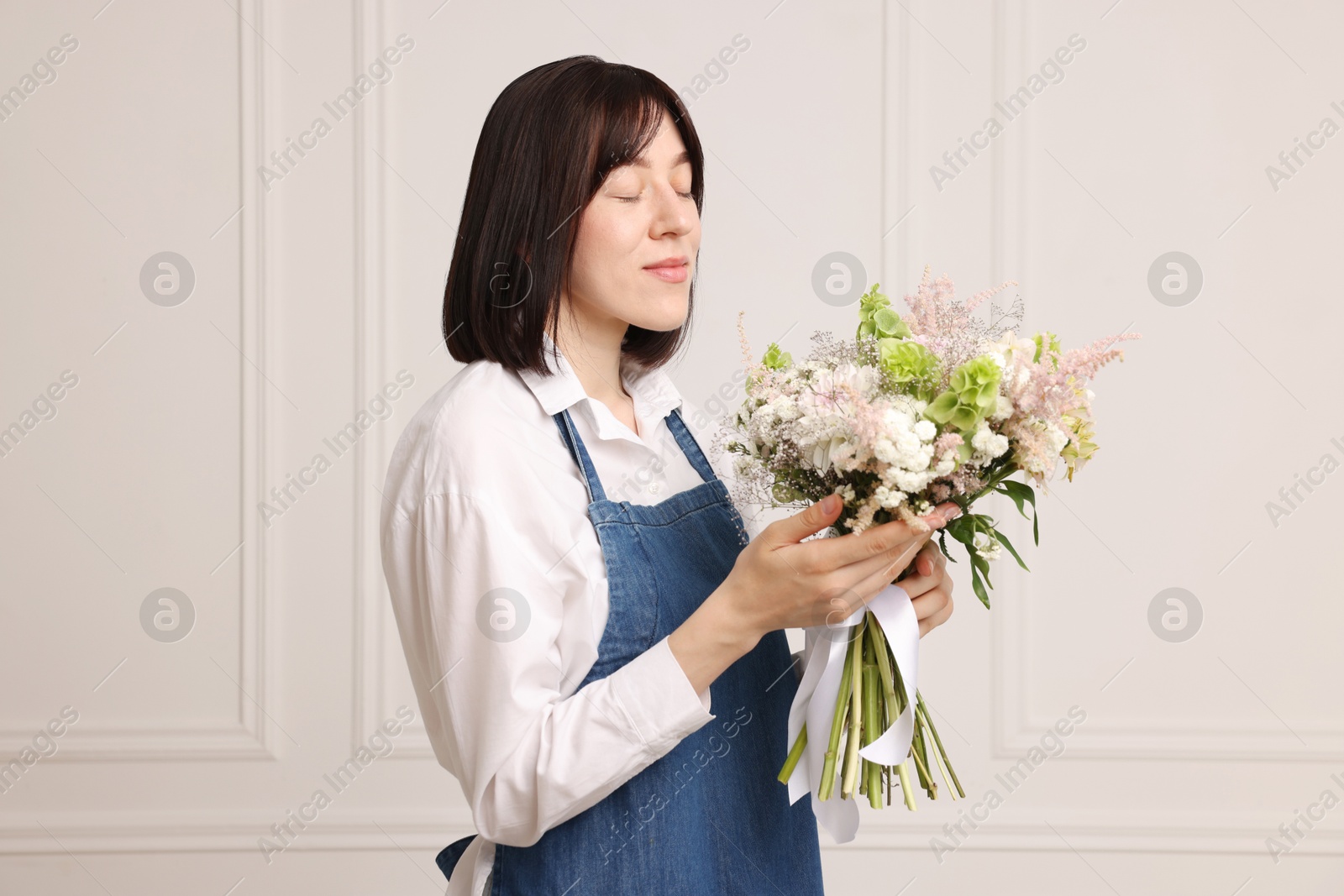 Photo of Florist with beautiful bouquet of flowers near white wall indoors