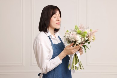 Photo of Florist with beautiful bouquet of flowers near white wall indoors