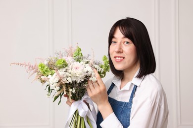 Photo of Florist with beautiful bouquet of flowers near white wall indoors