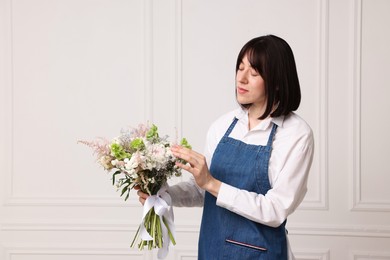 Photo of Florist with beautiful bouquet of flowers near white wall indoors