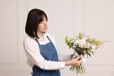 Photo of Florist with beautiful bouquet of flowers near white wall indoors