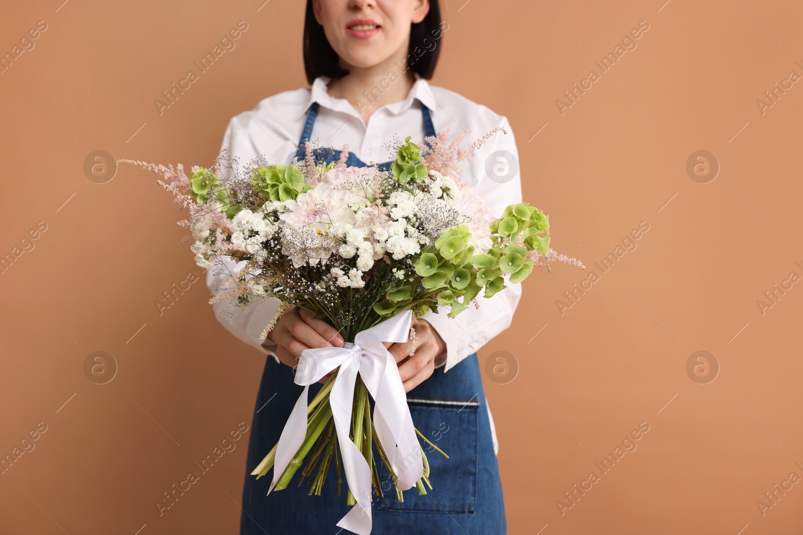 Photo of Florist with beautiful bouquet of flowers on dark beige background, closeup