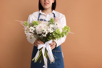 Photo of Florist with beautiful bouquet of flowers on dark beige background, closeup