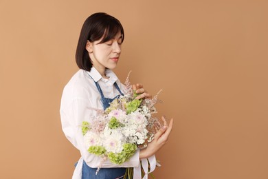 Photo of Florist with beautiful bouquet of flowers on beige background, space for text