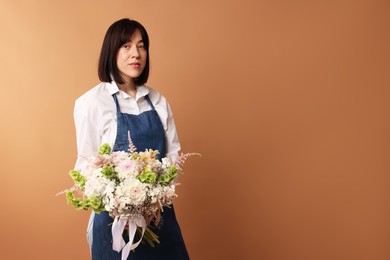 Photo of Florist with beautiful bouquet of flowers on dark beige background, space for text
