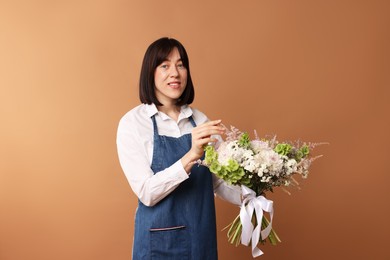 Photo of Florist with beautiful bouquet of flowers on dark beige background